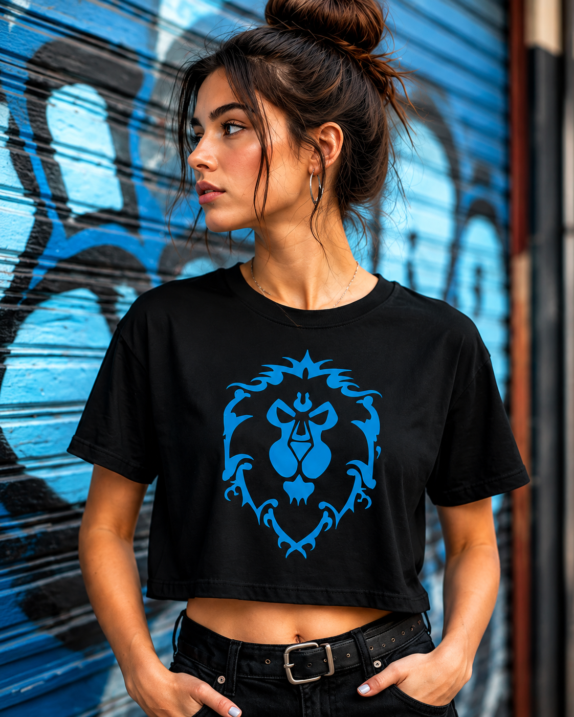 A woman wearing a black cropped t-shirt with a blue World of Warcraft Alliance Crest graphic, standing in front of a blue graffiti metal shutter.