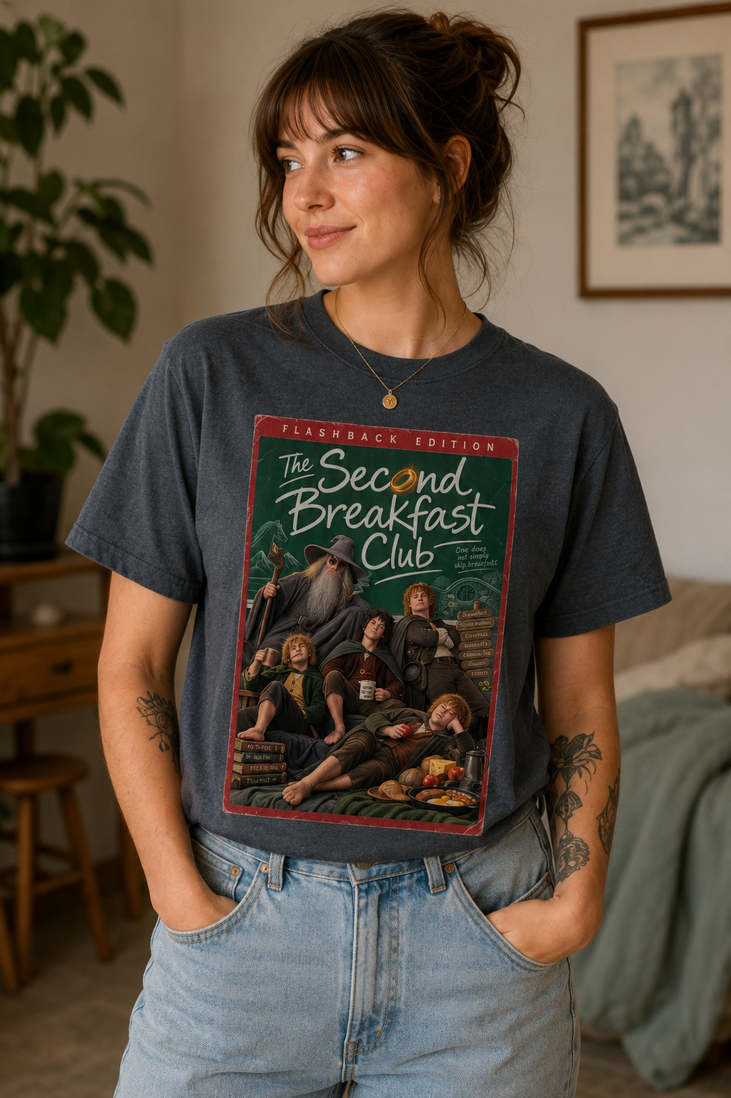 A woman wearing an blue short-sleeve lord of the rings t-shirt with a large graphic print on the front featuring character parody of 'The Second Breakfast Club' in a vintage comic-book / dvd video style. The graphic includes the text 'FLASHBACK EDITION' and 'The Second Breakfast Club'.